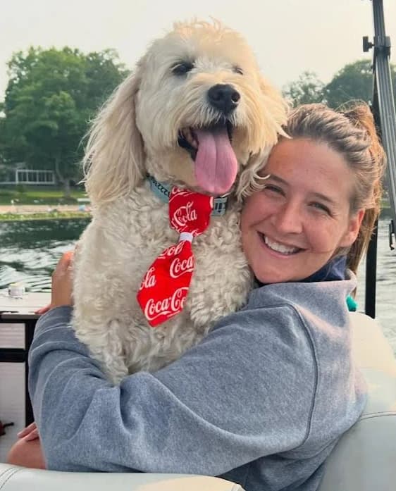 Dunkin the golden doodle in a red tie, getting a hug on a boat